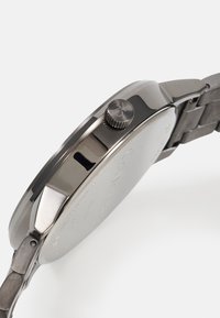 Edelstahlarmbanduhr mit rundem Gehäuse, strukturiertem Krone und matter Oberfläche. Verfügt über ein mehrschichtiges Metallarmband.