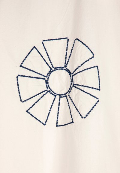 Tessuto bianco con motivo geometrico ricamato in blu navy, caratterizzato da un cerchio centrale circondato da segmenti allungati. Dettaglio di cucitura testurizzata.