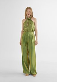Top halter de satén verde con detalle de ojal, combinado con pantalones verdes de pierna ancha y cintura alta, que presentan un ligero brillo y un ajuste entallado.