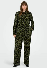 Dvoudílný outfit s černým základem a zeleným abstraktním vzorem. Halenka má dlouhé rukávy a detaily ve tvaru klíčové dírky; kalhoty mají široké nohavice.