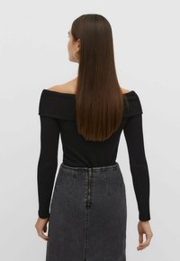 Schwarzes, geripptes Off-Shoulder-Oberteil, kombiniert mit einem hoch taillierten grauen Denim-Rock mit Reißverschluss auf der Rückseite. Langes, glattes Haar.