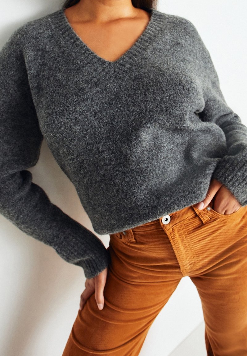 Šedý vlněný svetr s výstřihem do V, žebrovanými manžetami a uvolněným střihem, spárovaný s kalhotami z kordu v barvě rezavě hnědé s předními kapsami.