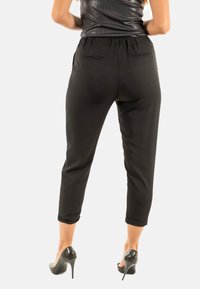 Pantalones recortados negros con una cintura elástica, dos bolsillos traseros y una textura suave, combinados con tacones altos brillantes.