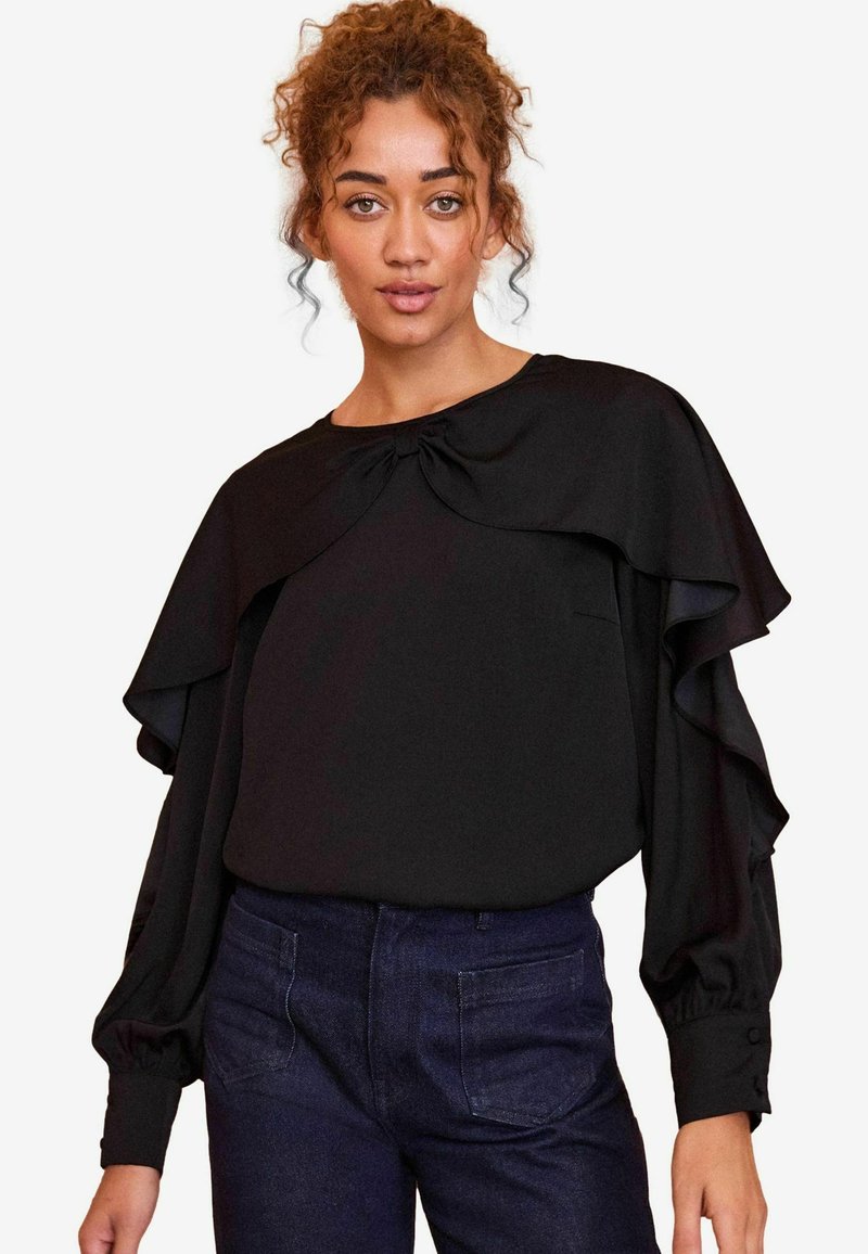 Blusa nera con maniche a strati a volants, scollatura tonda e dettaglio a fiocco sul davanti. Tessuto liscio con una leggera lucentezza.