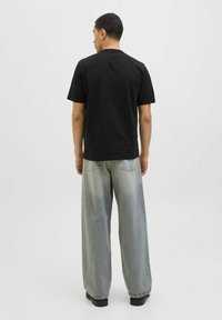 Sort bomulds T-shirt med korte ærmer og rund hals, parret med lyseblå, brede denimbukser, set bagfra.