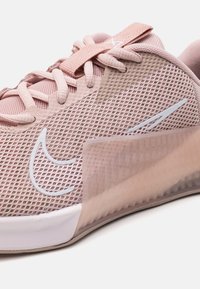 Scarpa sportiva rosa chiaro con tomaia in rete, suola in gomma e dettagli bianchi. Presenta un design testurizzato e chiusura con lacci per una vestibilità sicura.
