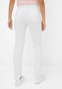 Witte strakke broek met een gladde textuur, voorzien van twee achterzakken en een recht model. Gecombineerd met witte sneakers.