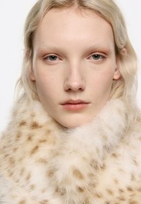 Cuello de piel beige con manchas de leopardo, con una textura suave y un brillo sutil. Primer plano de un rostro con piel clara y cabello de color claro.