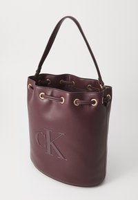 Borsa a secchiello in pelle bordeaux con hardware dorato, logo impresso e chiusura con coulisse. Presenta un manico singolo e una finitura morbida e testurizzata.