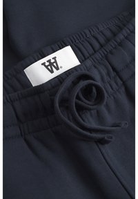 Navy blue cotton sweatpants featuring an elastic waistband, adjustable drawstring, and a small white label with a black logo.