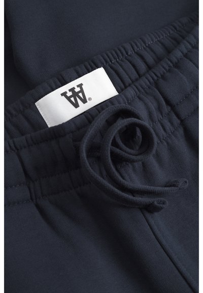 Pantalons de survêtement en coton bleu marine avec une ceinture élastique, un cordon de serrage ajustable et une petite étiquette blanche avec un logo noir.