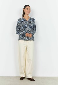 Bluza cu imprimeu floral în bleumarin, albastru deschis și crem, cu mâneci lungi și decolteu în V; asortată cu pantaloni largi crem și pantofi comozi închis la culoare.