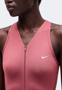 Gros plan d'une personne portant un haut de sport rose sans manches à fermeture éclair avec un logo blanc Nike sur le côté gauche de la poitrine.