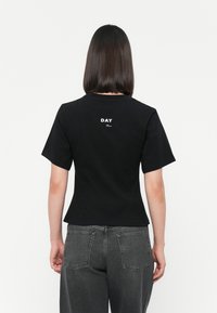 Black short-sleeve top with a fitted design, featuring a white "DAY" print on the back. Smooth cotton material, plain texture, minimal accents.