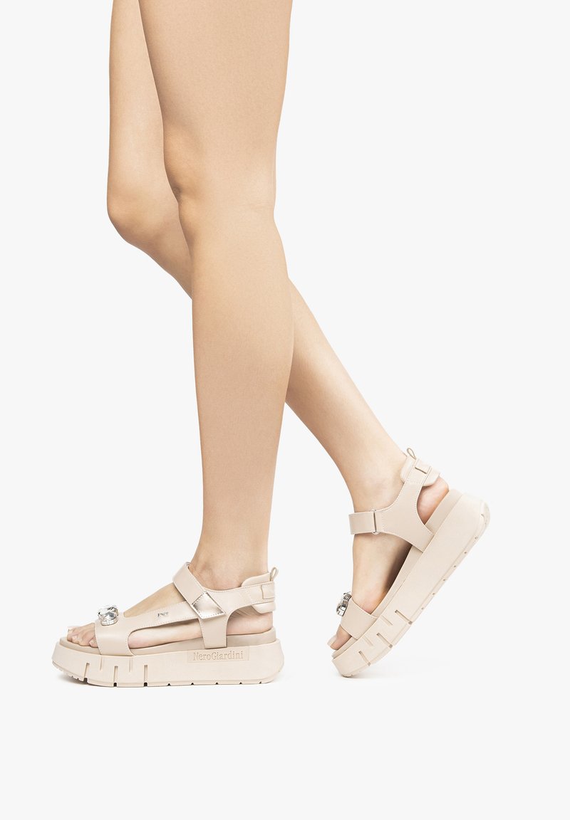 I sandali piatti beige presentano fasce larghe, dettaglio con fibbia e suola in gomma con scanalature testurizzate. Progettati con punta aperta e vestibilità regolabile.