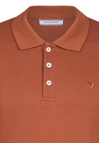 Polo de couleur rouille en tissu texturé, avec un col, une patte de boutonnage à trois boutons et un logo d'oiseau brodé sur la poitrine.