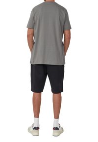 Grauer Baumwoll-T-Shirt mit kurzen Ärmeln, kombiniert mit schwarzen Shorts. Weiße Sneakers mit farblichen Akzenten und weißen Crew-Socken. Einfaches Design.