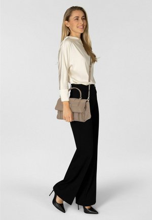 Bolso de mano beige claro con solapa cosida y herrajes plateados, combinado con una blusa crema y pantalones anchos negros, presentado sobre un fondo gris.