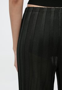 Fekete, függőleges csíkos nadrág, áttetsző, könnyű anyagból készült, elasztikus derékrésszel és testhez simuló szabással.