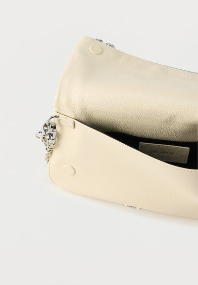 Krémová kožená taška s textúrovaným povrchom, zapínaním na zips a kovaniami v striebornej farbe. Vo vnútri je viditeľná štítok, dizajn má zaoblené rohy.