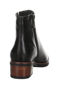 Botín de cuero negro con cremallera lateral, puntera ligeramente redondeada y tacón de madera en contraste. Textura suave con acentos mínimos.