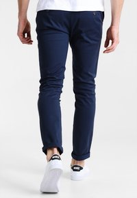 Tmavě modré slim fit kalhoty vyrobené z elastické tkaniny, s hladkým povrchem, mírně ohrnutými manžetami a kontrastním hnědým knoflíkem.