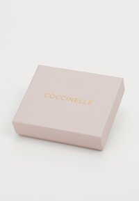 Boîte d'emballage Coccinelle en rose doux avec une finition mate. Présente un logo gaufré doré sur le dessus et une forme rectangulaire.