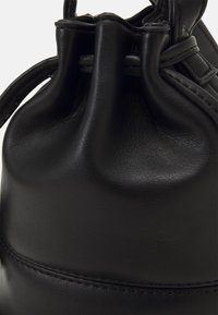 Borsa a tracolla in pelle nera con una texture liscia, cima arricciata e dettagli di cucitura sottili lungo il bordo inferiore.