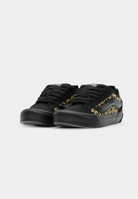 Svarte sneakers med en leopardmønsterdetalj på siden, teksturert stoff, flate såler og tykke svarte skoøyer for sikker passform.