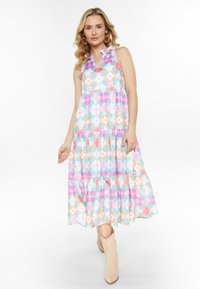 Florales Maxikleid in Pastellfarben, mit einem gestuften Design, Rüschenträgern und einem V-Ausschnitt. Getragen mit hellbeigen Stiefeletten.