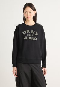 Svart bomullssweatshirt med "DKNY JEANS 1989" i metallisk skrift. Rund hals, ribbestrikkede mansjetter og en avslappet passform. Glatt tekstur.