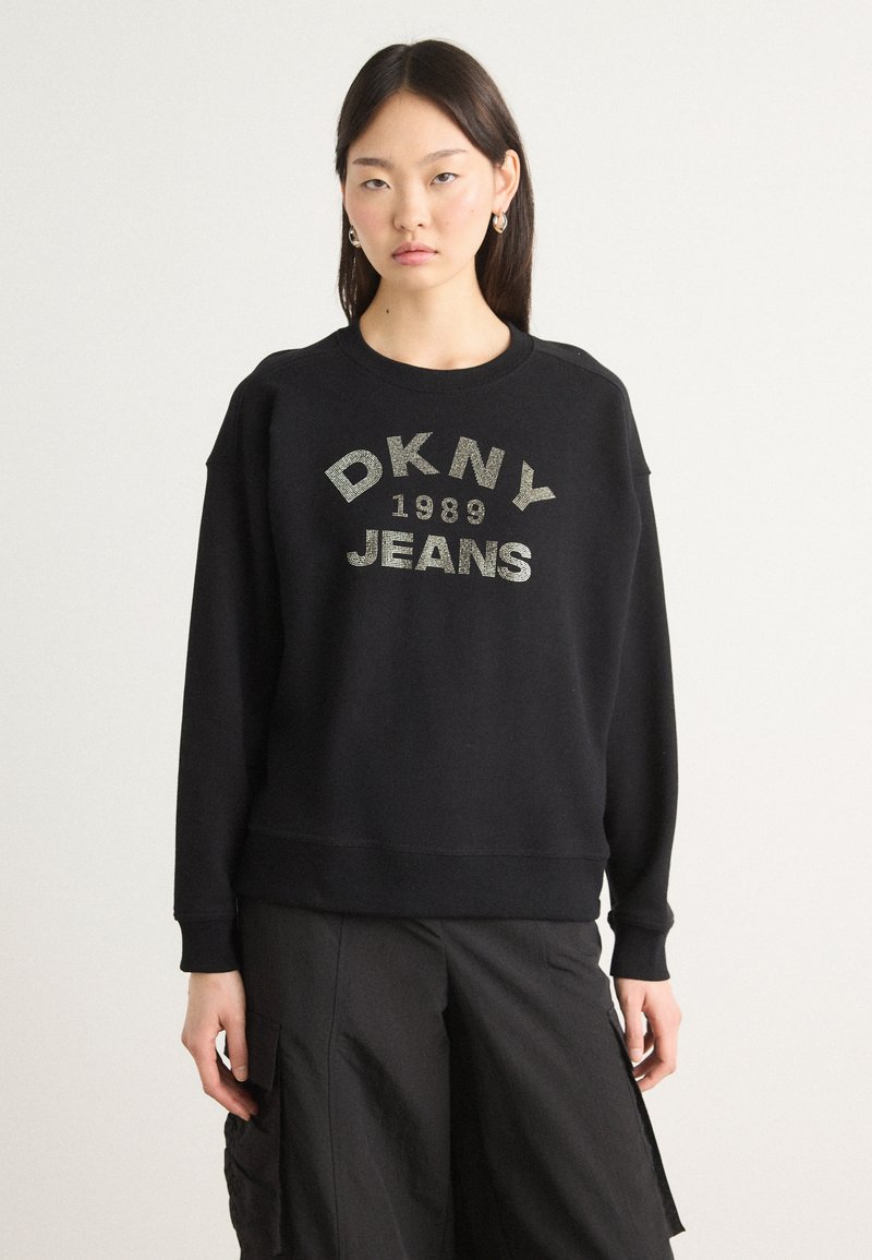 Svart bomullssweatshirt med "DKNY JEANS 1989" i metallisk skrift. Rund hals, ribbestrikkede mansjetter og en avslappet passform. Glatt tekstur.