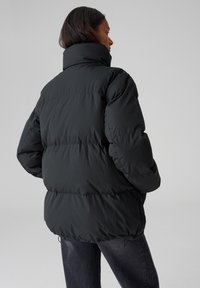 Giubbotto imbottito nero con colletto alto, caratterizzato da un design trapuntato e polsini elasticizzati. Texture morbida con una vestibilità leggermente oversize.