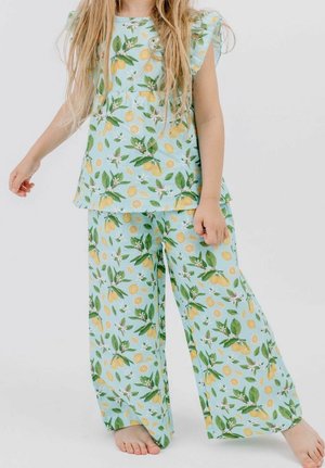 Child wearing light blue pajama set with lemon and leaf pattern, long pants, and short-sleeved top, standing barefoot on white background.