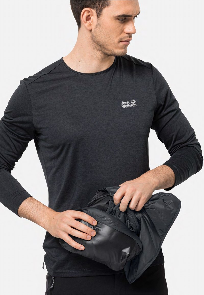 Schwarzes Langarm-T-Shirt mit kleinem weißem Logo; das Modell hält eine kompakte schwarze isolierte Jacke; glatte Textur.