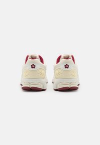 Białe i bordowe buty sportowe z siateczkowych i gumowych materiałów, z teksturowanym wzorem z tyłu oraz akcentem w postaci logo na pięcie.