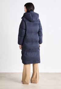 Jūras spēku garš pūkains mētelis ar kapuci, ar quilted dizainu un pārlieku lielu izmēru. Iespējas sānu šķelšanās un matēta tekstūra, kas nodrošina siltumu un komfortu.
