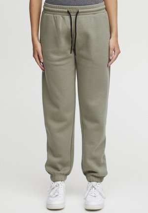 Olivengrønne joggebukser med elastisk mansjett, justerbar svart snor og sidelommer, kombinert med hvite sneakers. Myk bomullsblandingsmateriale.