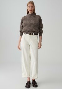 Maglione marrone a maglia grossa con colletto alto, abbinato a pantaloni palazzo color crema e mocassini scuri. Design semplice, vestibilità rilassata.