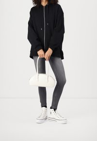 Svart zip-up oversized hoodie, grå skinny jeans, vita plattformssneakers och en vit handväska med kurvig form och korta handtag.