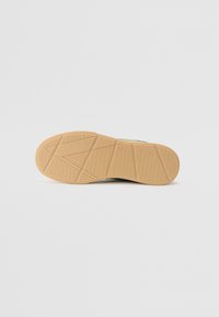Sneakerzool van een getextureerd gumrubber materiaal, met een zigzagpatroon en meerdere gripsecties, ontworpen voor grip op verschillende oppervlakken.