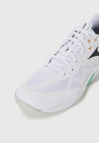 White athletic shoe with mesh and synthetic material, featuring a textured design, black accents, and a translucent rubber sole.