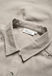 Beige corduroy shirt featuring a folded collar, silver snap buttons, and a label reading "KAREN BY SIMONSEN." Textured fabric visible.