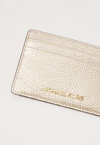 Portofel de carduri din piele texturată aurie, cu multiple sloturi și numele mărcii "MICHAEL KORS" embosat în aur. Design compact.