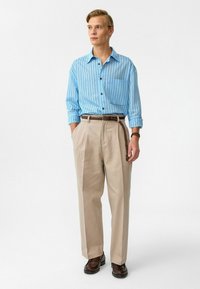 Lichtblauw gestreept overhemd met een zak, gecombineerd met beige geplooide broek en een gestructureerde bruine riem; bruine schoenen maken de outfit compleet.