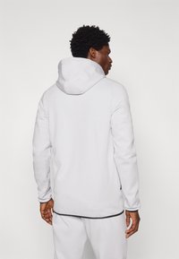 Λευκό μπουφάν με κουκούλα και λεία υφή, με άνετη εφαρμογή και μαύρες αντιθέσεις κατά μήκος του τελειώματος και των μανσέτων.