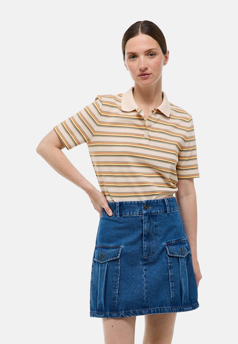 Polo-shirt à rayures horizontales beige, orange et verte, associé à une jupe en denim bleu avec poches avant et fermeture à boutons.