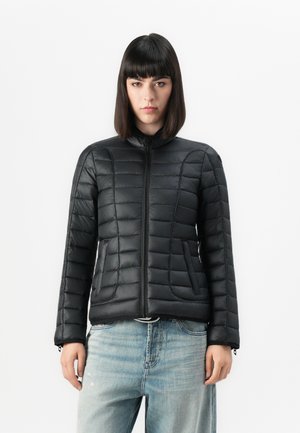 Zwarte pufferjas met een hoge kraag, horizontale stiksels en een rits aan de voorkant. Bevat zijzakken en verstelbare manchetten. G gedragen met lichte denim.