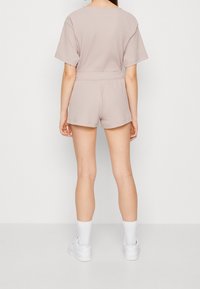 Kvinna som står vänd bortifrån iförd en ljus mauve ribbad kortärmad topp och matchande shorts med vita strumpor och sneakers.