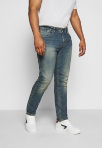 Jeans de corte skinny en un lavado azul deslavado, con diseño de cinco bolsillos y sutiles desgastes. Combinados con zapatillas blancas.